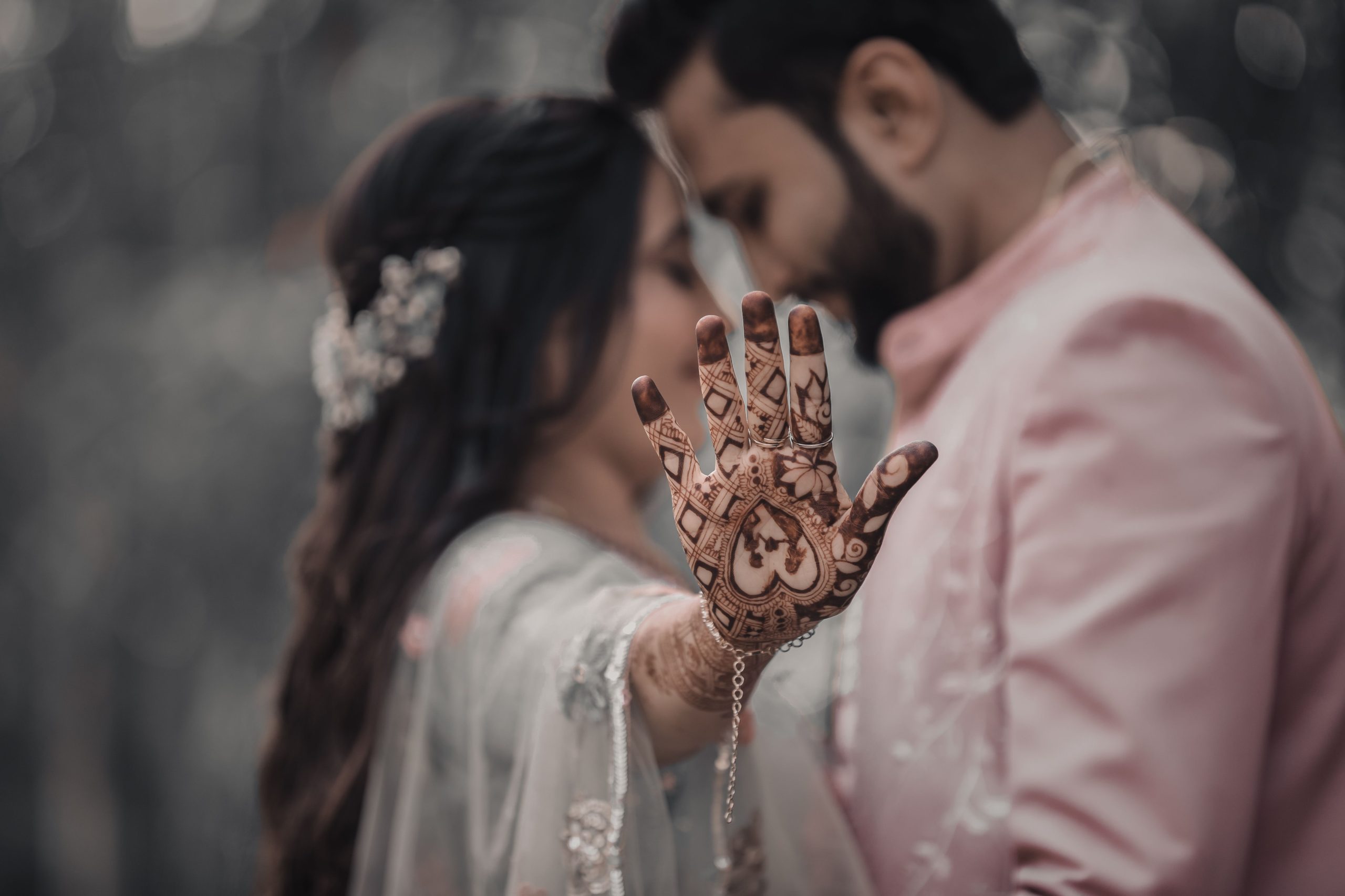 Close-up of a bride showing mehndi on her hand while embracing her groom, symbolizing love and tradition.